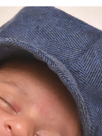 A detailed shot of a baby's face, partially covered by a stylish blue cap. It highlights the texture of the fabric and the baby's soft, sleeping features.