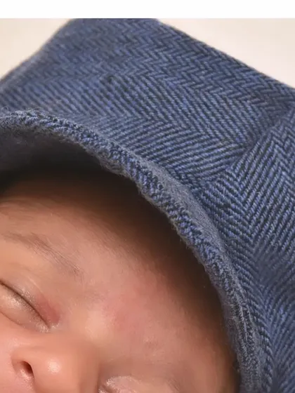 A detailed shot of a baby's face, partially covered by a stylish blue cap. It highlights the texture of the fabric and the baby's soft, sleeping features.