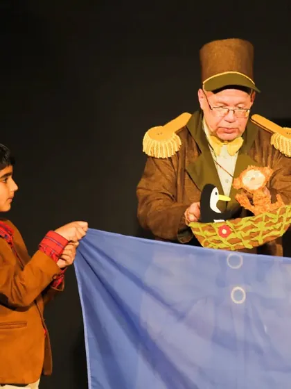 The puppeteer from 'Penguin in my Pocket' invites a young boy from the audience to help with the show, making the performance an interactive and engaging experience.