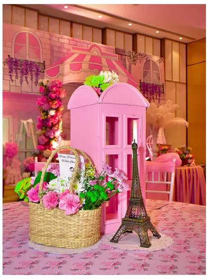 A beautiful tablescape from the Parisian party, featuring a miniature Eiffel Tower, a basket of flowers, and a pink telephone booth prop.