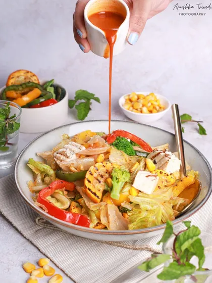 A healthy and colourful salad with grilled chicken and vegetables. The action of pouring the dressing adds a dynamic element to this fresh and vibrant shot.