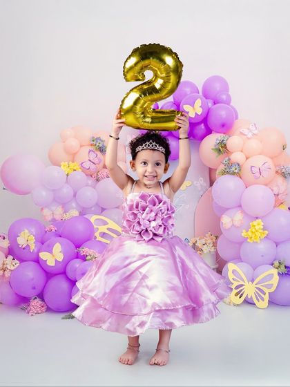 Holding up her new number with pride. This little princess is celebrating turning two surrounded by a cascade of purple and pink balloons.