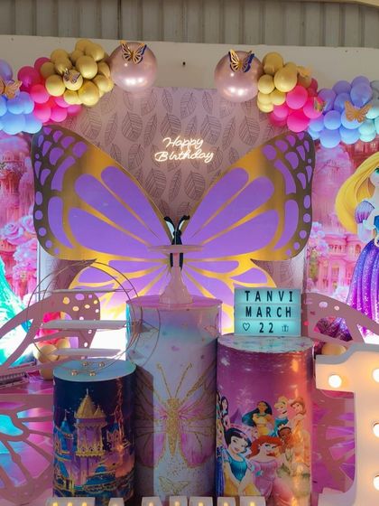A closer look at the princess and butterfly theme, showing the detailed custom plinths and the 'Happy Birthday' neon sign.