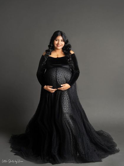 A full-body portrait showcasing an elegant black velvet and tulle gown. The mother-to-be smiles warmly, her hands on her bump, in this classic and sophisticated studio shot.