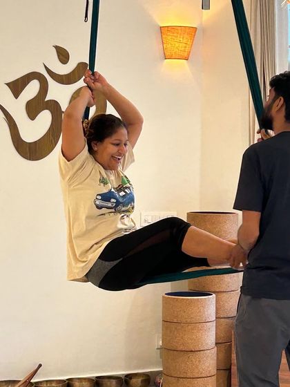 An instructor assists a student in an aerial pose, highlighting the personalized attention and supportive community at our Yogshala.