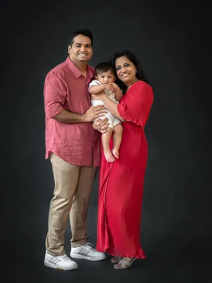 A classic family-of-three portrait against a dark backdrop. This timeless style is perfect for celebrating a milestone like a first birthday.
