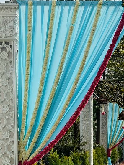 A close-up of our drape work, showing how we combine fabrics like this light blue material with traditional jasmine garlands. The pink floral border adds a pop of color to the wedding entrance.