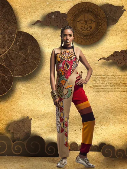 A creative fashion photograph featuring a unique jumpsuit with asymmetrical leg patterns. The model's confident stance and the artistic backdrop come together to tell a story of bold, modern design rooted in tradition.