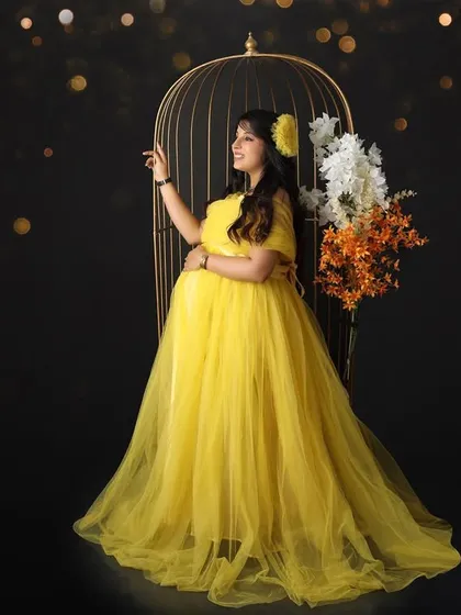 You are meant to shine. This portrait features a mom-to-be in a bright yellow gown, standing next to a decorative birdcage, surrounded by a magical bokeh effect.