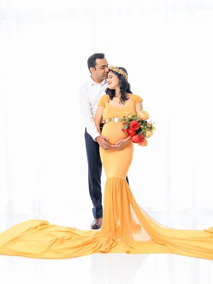 A classic and elegant couple's portrait. The mom-to-be holds a bouquet of flowers while wearing a beautiful yellow gown, creating a soft and romantic look.