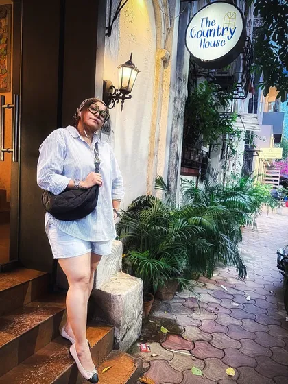 A casual yet stylish look with an oversized striped shirt, shorts, and a headscarf, pictured outside 'The Country House' cafe.