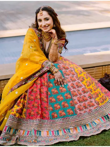 A beautiful portrait of the bride sitting by the pool, her colorful Mehendi lehenga spread out, looking radiant and happy.