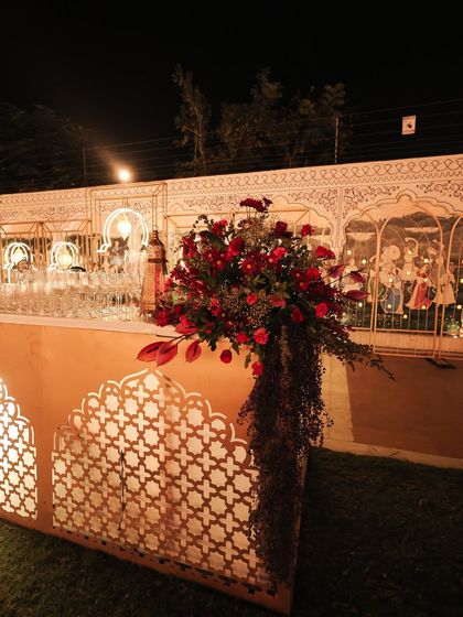 A beautifully styled bar for the Sufi sangeet, featuring an illuminated jali facade and a cascading floral arrangement in deep burgundy and plum tones, tying into the event's Moroccan theme.