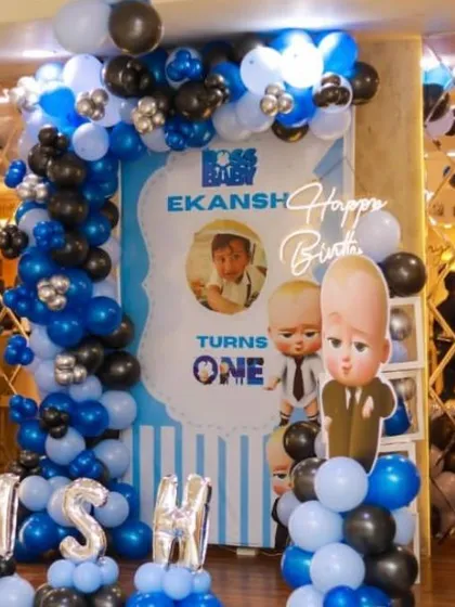 A "Boss Baby" themed first birthday party. The decor features character cutouts, a custom backdrop, and a blue, black, and silver balloon arch, perfectly executing this popular theme.
