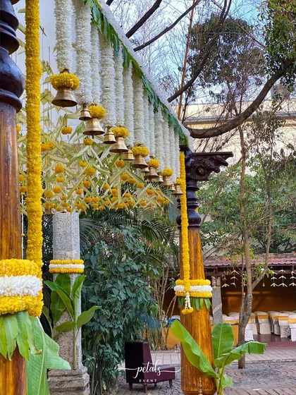 The beauty of a traditional South Indian wedding lies in its details. I adorned these majestic wooden pillars with garlands of white chrysanthemums and marigolds, adding cascading temple bells that chimed with every gentle breeze.