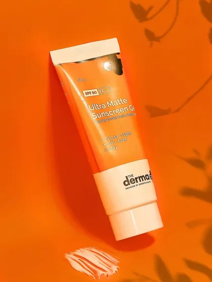 A flat lay of The Derma Co's sunscreen with a smear of the product shows its texture. The use of shadow play on a bold orange background creates a modern, graphic look for the brand.