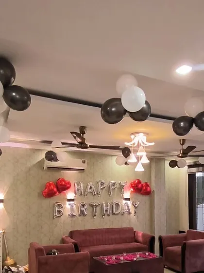 A living room decorated for a birthday with black and white balloon bunches, a 'Happy Birthday' banner, and rose petals on the coffee table.