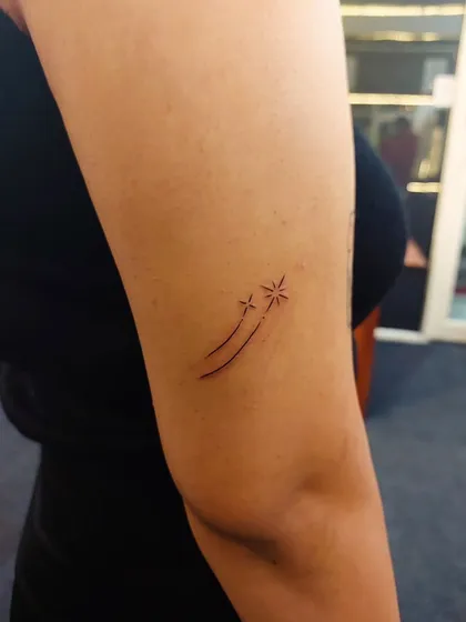 A pair of shooting stars created with fine lines and simple starbursts. This delicate arm tattoo is a magical and hopeful design.