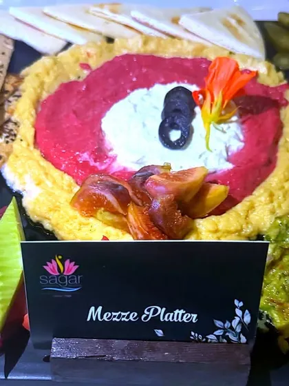 This vibrant Mezze Platter is perfect for sharing. It includes a trio of dips like classic hummus, beetroot hummus, and guacamole, served with soft pita bread, crackers, and fresh vegetables.