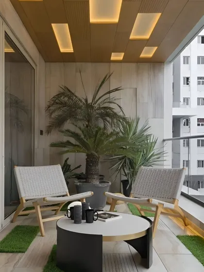 A modern balcony design with stylish wicker-back chairs and a compact coffee table. The space is finished with artificial grass patches and elegant recessed ceiling lights, creating a chic urban retreat.