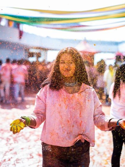 A guest smiles, covered in glitter and colored powder. I add unique touches like glitter to make my Holi parties extra special and memorable.