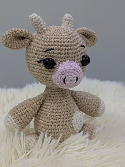 A gentle crochet cow in beige and white, with a soft pink nose.