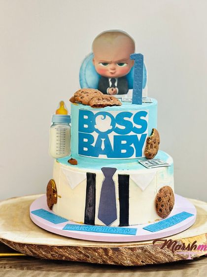 Here's a fun two-tiered Boss Baby theme cake for a first birthday. The bottom tier is designed to look like a shirt and tie, while the top features the Boss Baby himself, complete with edible money and cookies.