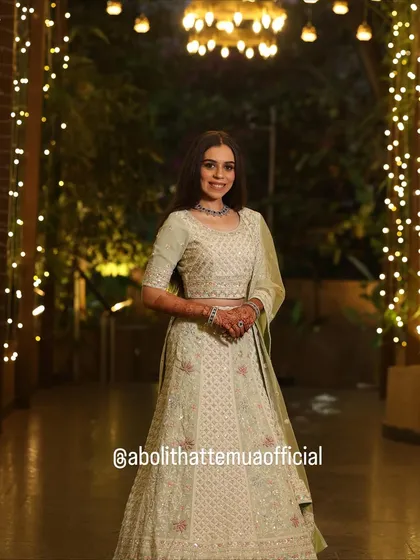 A full-length shot showcasing the elegant lehenga and hairstyle under beautiful fairy lights. The makeup is designed to look magical in evening lighting.