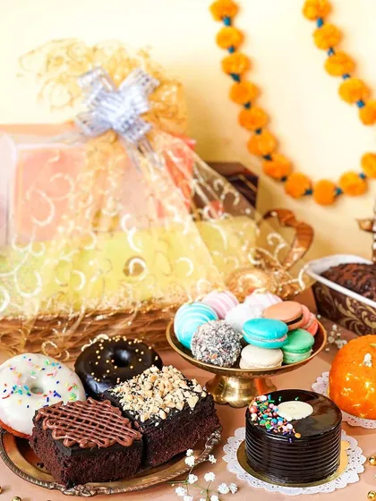 A festive hamper overflowing with baked goods like donuts, cakes, and macarons for Diwali. The traditional marigold garlands and diyas add an Indian festive touch to western desserts.