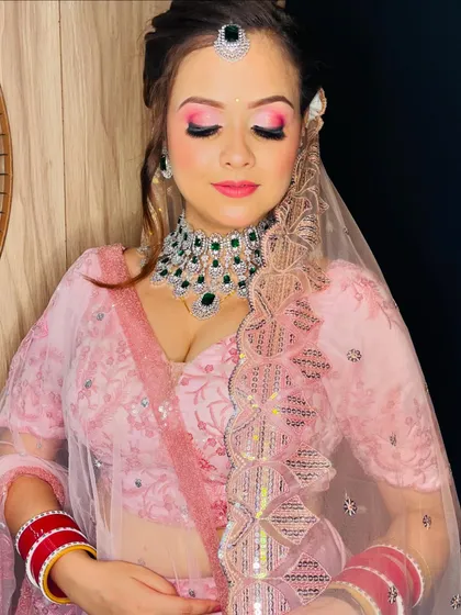 A modern bridal look with a soft pink lehenga and bright pink eyeshadow, paired with a diamond and emerald necklace.