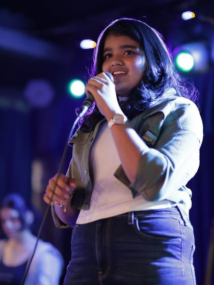 Confidence on stage is key. Here, one of our vocal students commands the microphone at our annual show. Our vocal coaching and ensemble practice build the skills to sing out loud and proud.