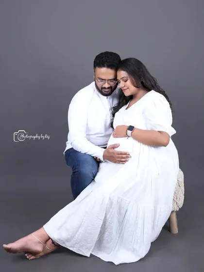 A tender studio portrait of a couple in matching white outfits, sharing a quiet moment of anticipation.