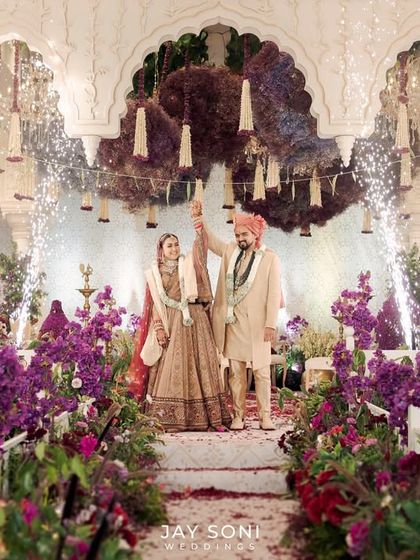 A moment of pure joy as the couple celebrates under the "Garden of Vows" mandap I designed. The aisle is lined with a lush meadow of purple and red flowers, leading to a stage that is both grand and deeply romantic.