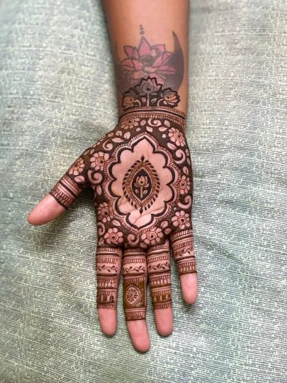 A unique cutwork design that incorporates a client's existing lotus tattoo, blending it seamlessly with the henna.