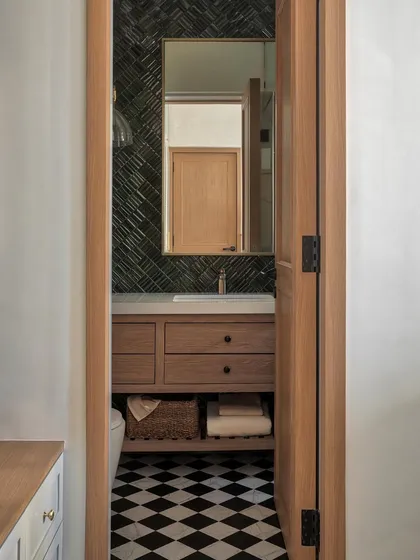 In this master bathroom, we opted for a custom chequerboard floor and arranged jade green tiles in a herringbone pattern for the standout wall. Gold-finish sanitary fittings from Kohler elevate the entire setting.