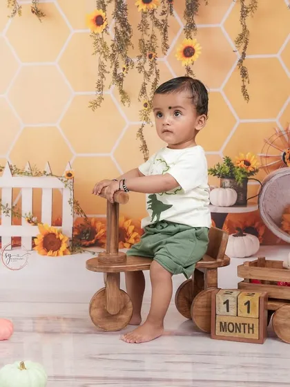 Celebrating 11 months with a sunny sunflower theme. This little one is enjoying his ride on a wooden tricycle in a cheerful, yellow setting.