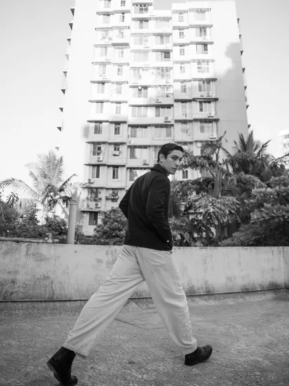 An outdoor, urban portrait in black and white. The low angle and the model's long stride create a dynamic, larger-than-life feel against the architectural backdrop.