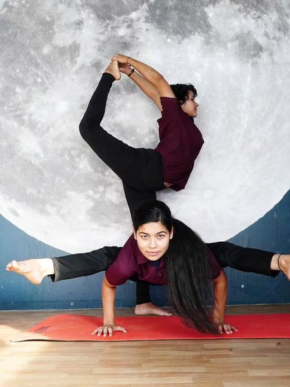 A stunning and creative two-person pose, blending an arm balance with a standing split variation.