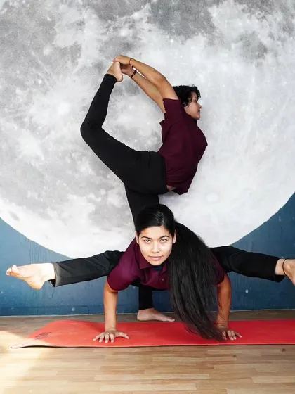 A stunning and creative two-person pose, blending an arm balance with a standing split variation.