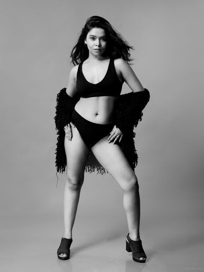 A powerful full-body monochrome portrait. The model's strong stance and the textured cardigan create a confident and fashionable image.