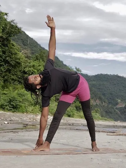 Utthita Trikonasana (Triangle Pose) practiced outdoors by the river in Rishikesh. This pose stretches the hamstrings, groins, and hips while also opening the chest and shoulders.