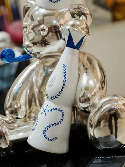 A close-up of the bottle and body of the silver "Let's Party Teddy," showing the reflective surface and detailed line work.