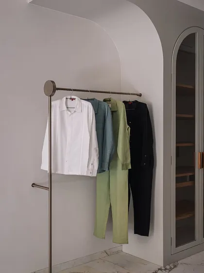 This walk-in wardrobe and bathroom was designed to feel like a high-end SoHo boutique. It features a sculptural, monolithic marble basin, an island dresser, and custom clothing racks, all set against a backdrop of luxurious veined marble.