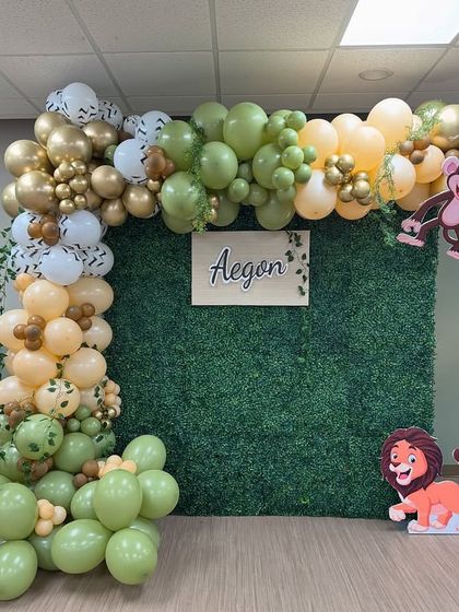 A 'Wild One' jungle-themed birthday party with a green hedge backdrop. The setup is decorated with an organic balloon garland and various animal props like a giraffe and zebra.