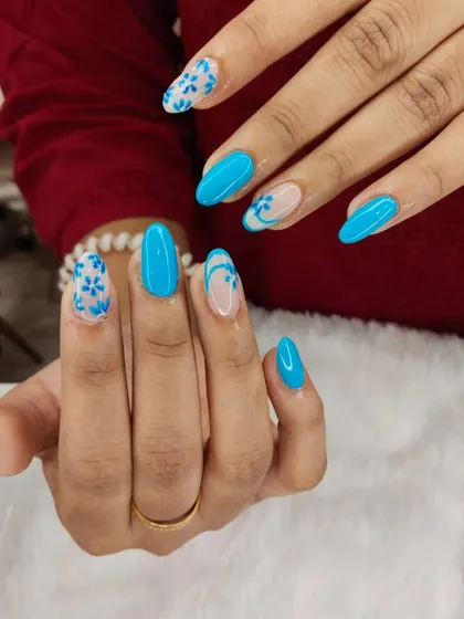 A beautiful design featuring a vibrant sky blue polish. The accent nails have delicate, hand-painted blue floral patterns on a sheer base for a light and airy feel.