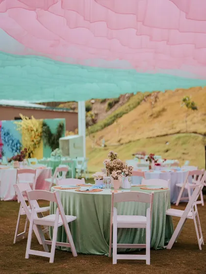 A sun-kissed Haldi lunch with tables draped in soft mint green linens under a canopy of pastel pink and mint fabric, creating a fresh and serene outdoor setting.