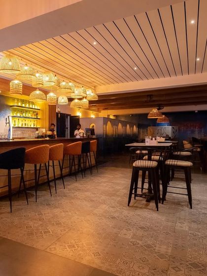 The bar at 'Sloshed' combines warm cane lighting with a cool blue color palette. This transformation created a spacious and inviting area with distinct zones for lounging and socializing.