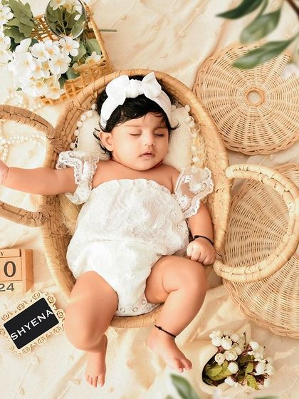 An overhead shot of a baby in a white lace romper, resting in a teacup-shaped wicker prop. This is a unique and charming take on a rustic theme.