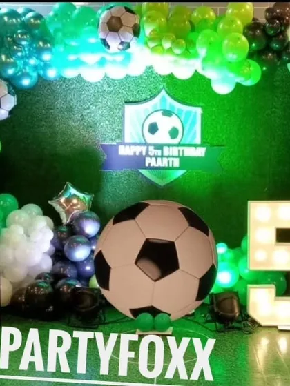 A football theme party setup with a giant football prop, a light-up number '5', and a green turf-like backdrop for a stadium feel.