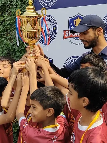 Lifting the trophy high. Our coach and the U10 team celebrate their championship win at the Gurgaon Youth League, a major achievement for our young squad.